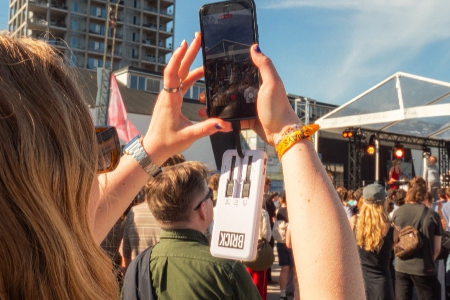 A festival crowd, one guest filming with a Brick powerbank on the phone