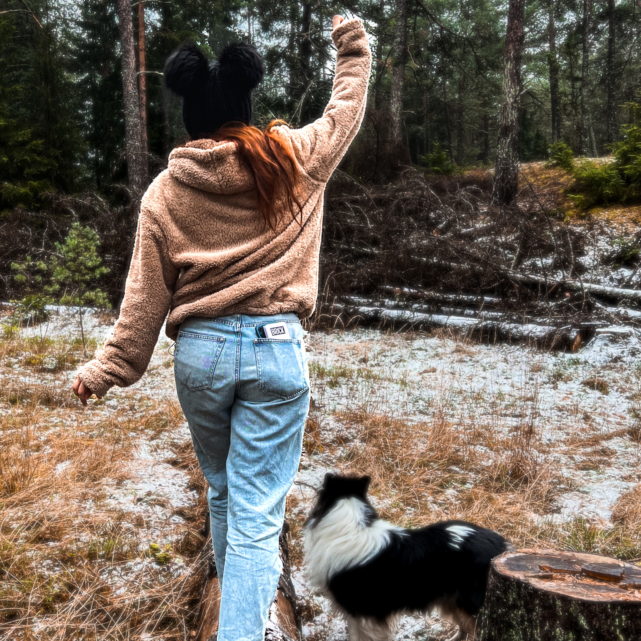 A girl with a Brick powerbank in her back pocket walking in a forest with a dog