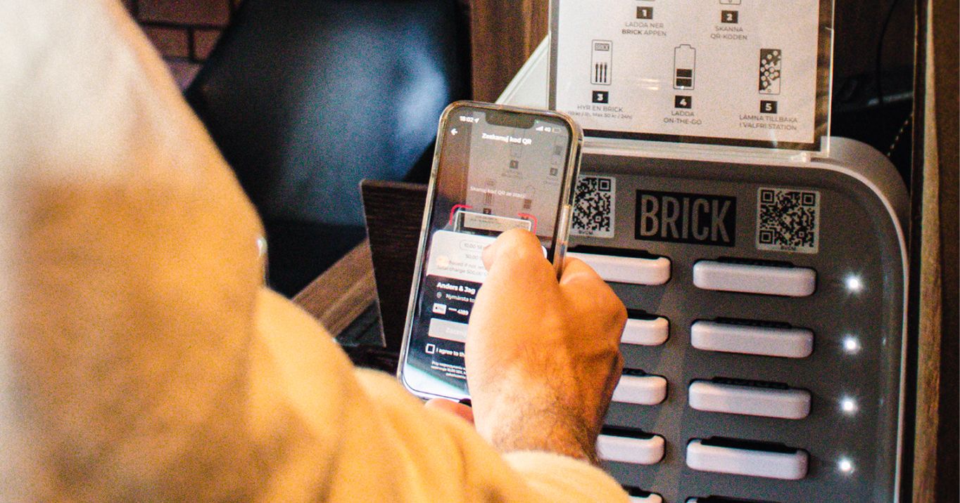 Person using an iPhone to scan the QR code on a 12 slot Brick powerbank sharing station