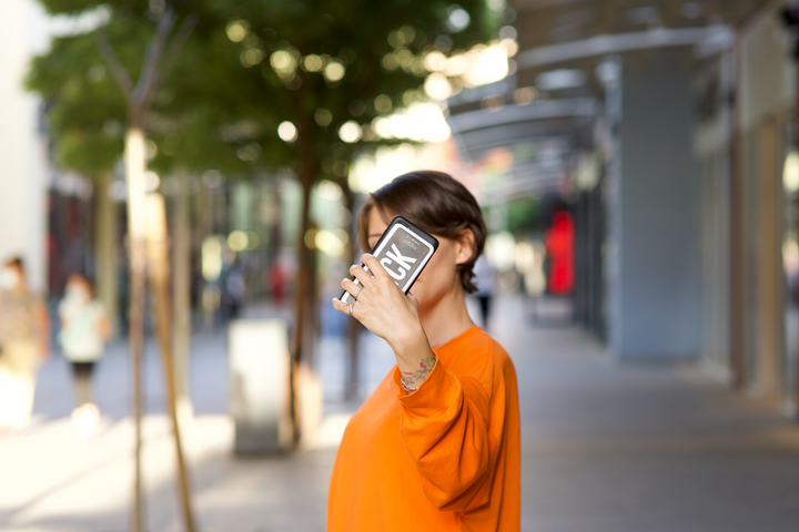 Girl in orange shirt, standing outside, holding up a Brick powerbank